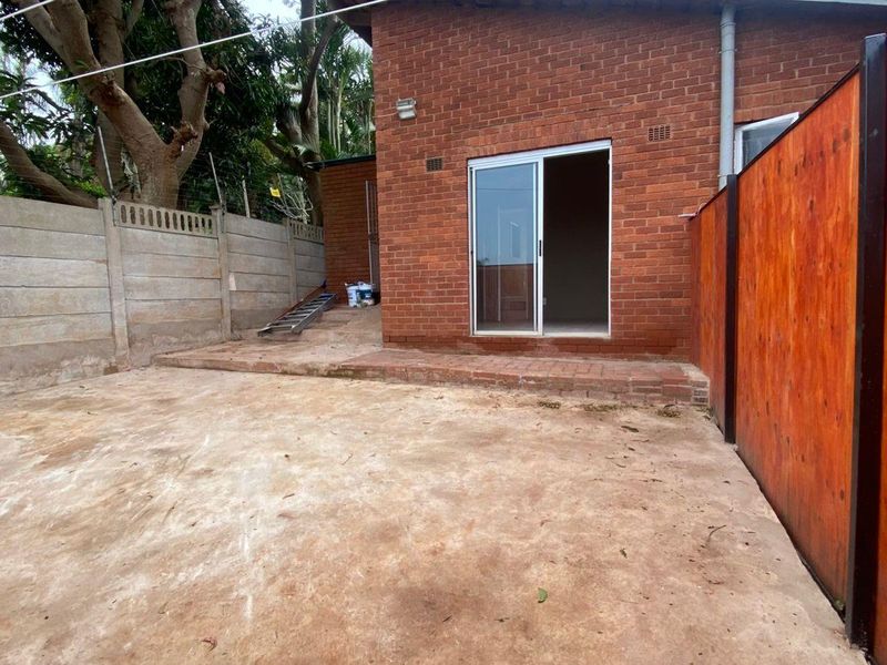 Rear exterior view of the cottage featuring a brick facade, sliding glass door access, and a concrete patio area enclosed by boundary walls.