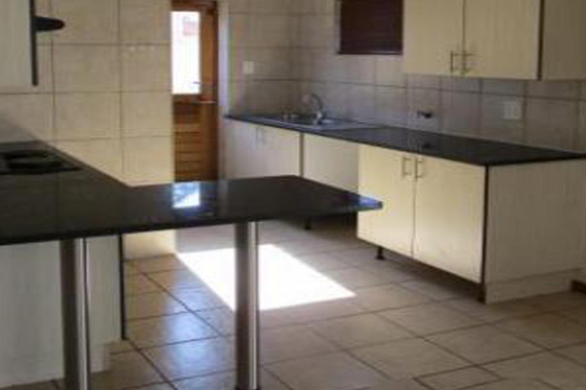 A functional kitchen featuring dark granite countertops, light-toned cabinetry, tiled flooring, and a breakfast bar peninsula with direct access to the exterior.