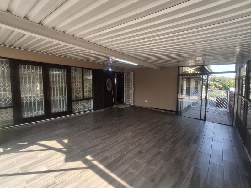 A spacious covered patio featuring modern wood-look floor tiles, corrugated metal roofing, and secure sliding glass door access to the main dwelling.