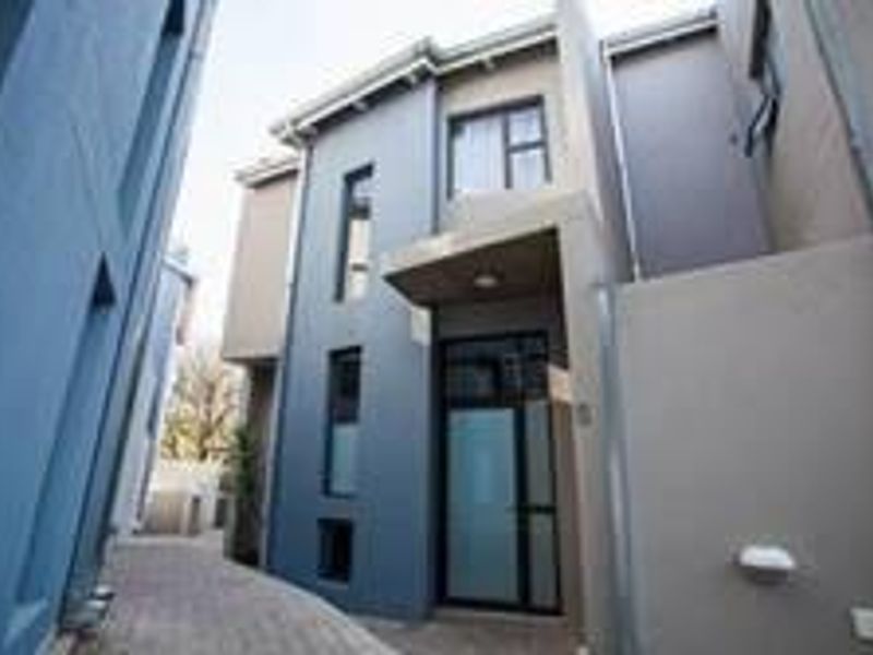A modern townhouse exterior featuring a paved walkway leading to a covered entrance with contemporary architectural finishes and aluminum window frames.