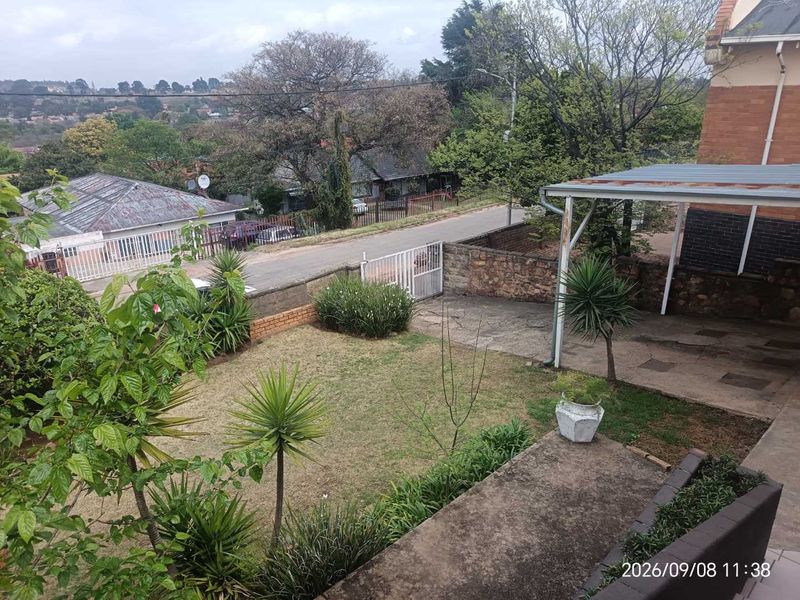A rear garden view featuring a lawn, stone boundary wall, and a covered patio area with metal support structures.