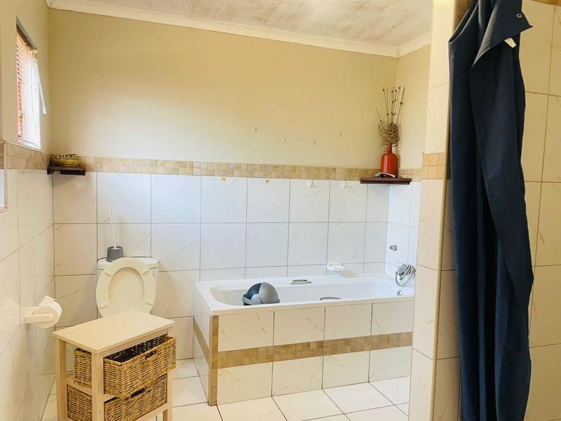 A functional bathroom featuring a built-in bathtub, toilet, and tiled finishes, requiring some maintenance and cosmetic updates to improve its overall condition.