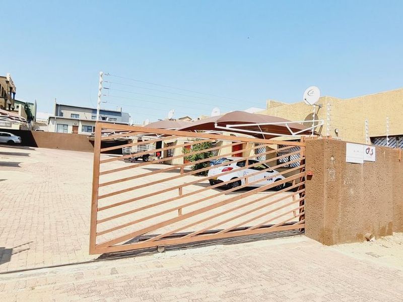 Front exterior view of the townhouse complex featuring a paved driveway, secure sliding gate, carport parking, and perimeter electric fencing.