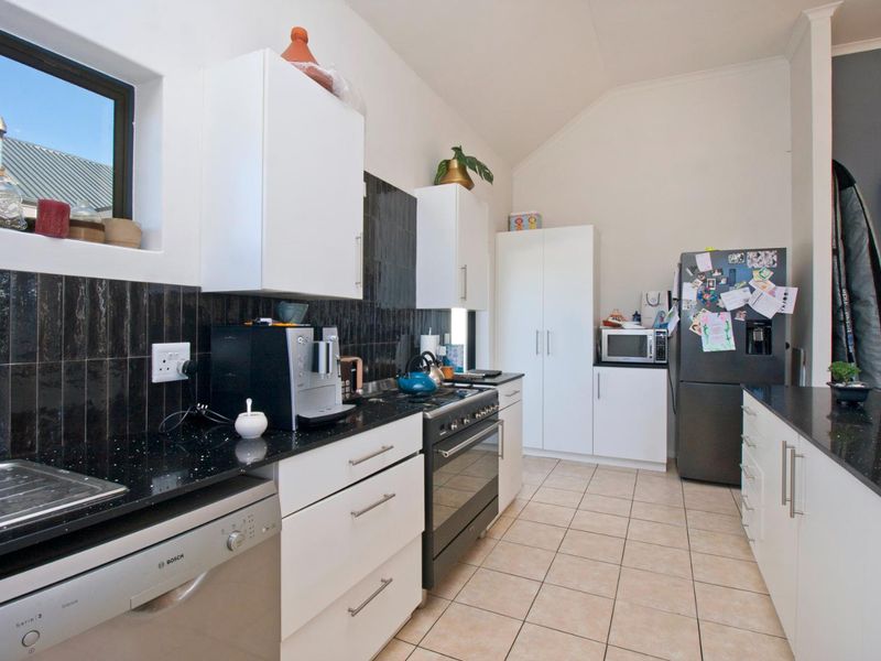 Modern kitchen featuring white cabinetry, black granite countertops, a black tiled backsplash, gas stove, and tiled flooring under a vaulted ceiling.