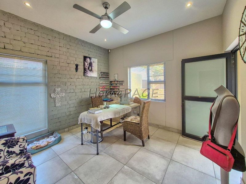 A versatile room featuring an exposed brick feature wall, tiled flooring, ceiling fan, and modern aluminium window frames, currently utilized as a workspace.