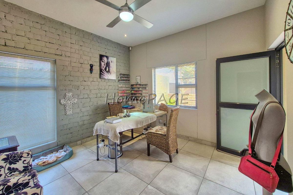 A versatile room featuring an exposed brick feature wall, tiled flooring, ceiling fan, and modern aluminium window frames, currently utilized as a workspace.