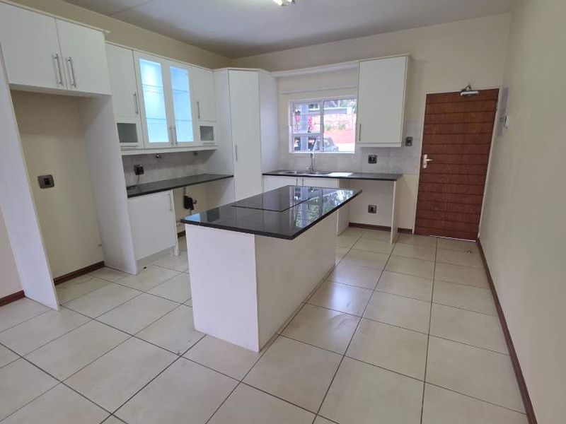 A bright, modern kitchen featuring white cabinetry, a central island with granite countertops, and neutral ceramic floor tiles.