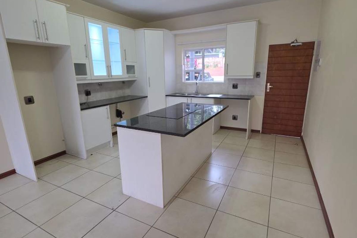 A bright, modern kitchen featuring white cabinetry, a central island with granite countertops, and neutral ceramic floor tiles.