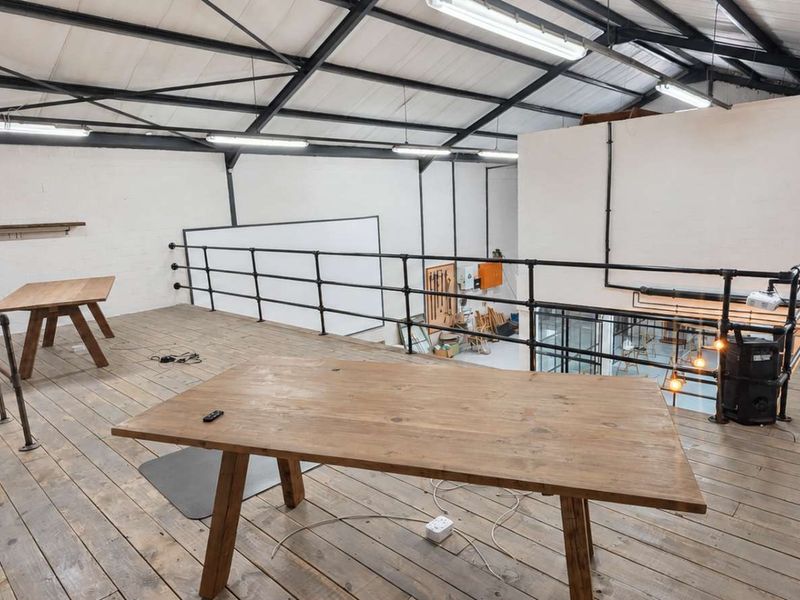 Spacious industrial-style mezzanine level featuring exposed steel roof trusses, timber flooring, and black pipe railings, offering an open and versatile workspace.