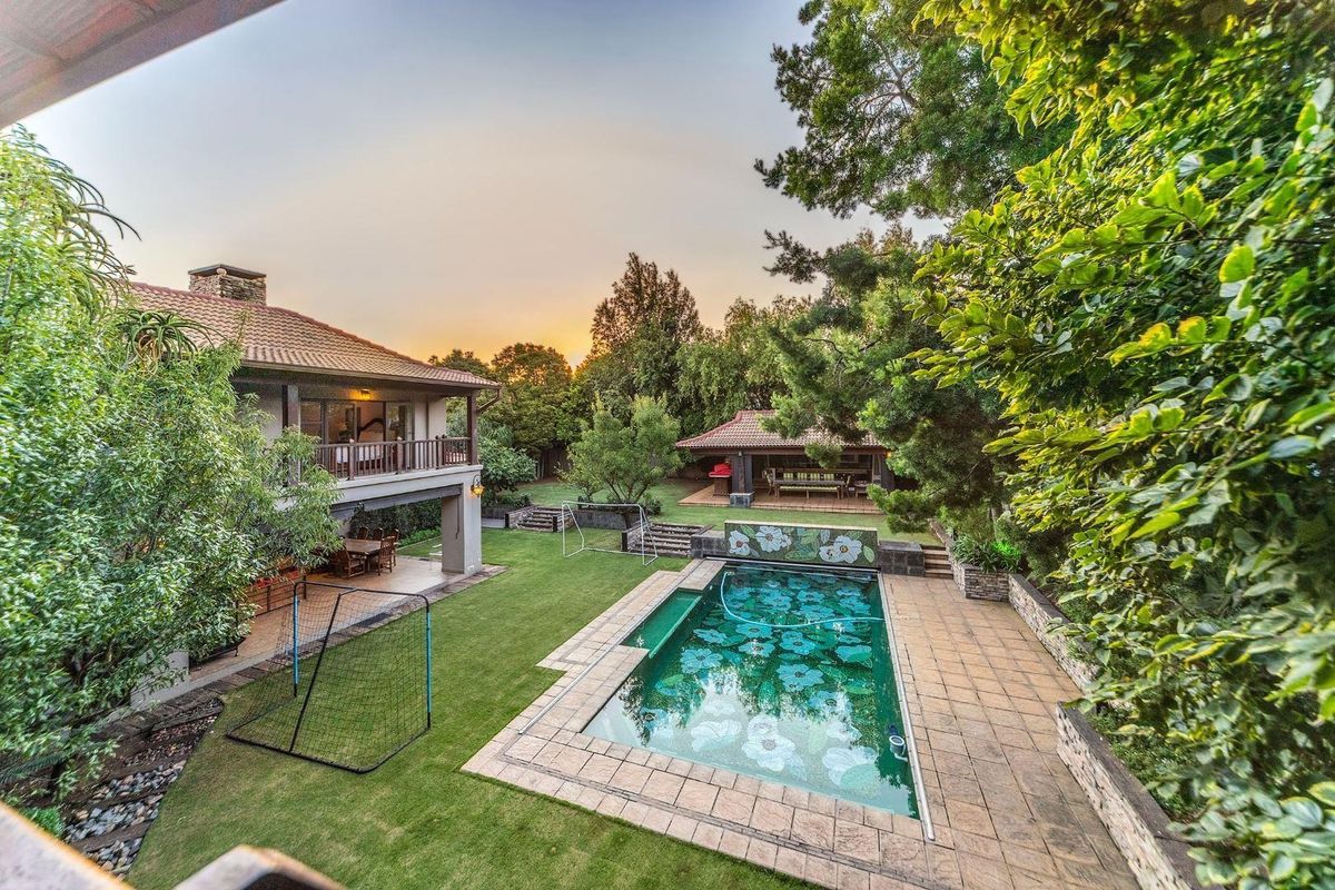 Spacious backyard featuring a swimming pool with decorative tiling, a manicured lawn, and a covered patio area attached to the main residence.