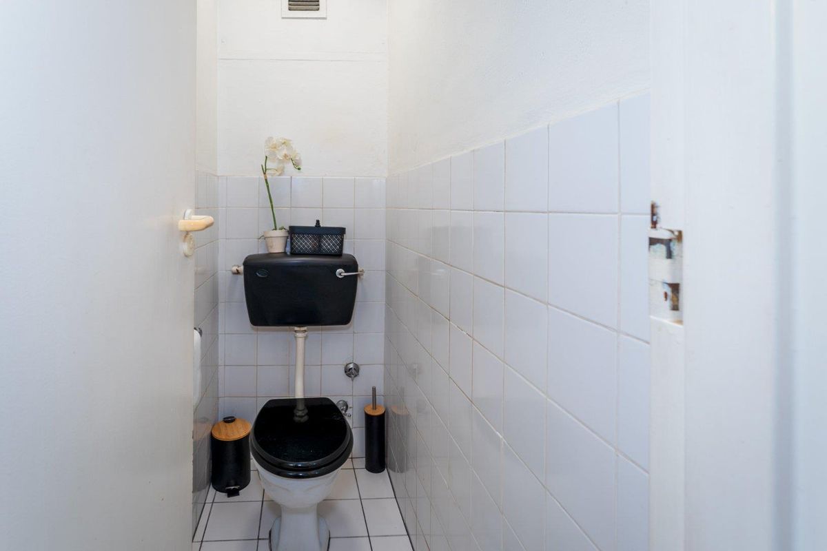 A compact guest bathroom featuring white wall tiles, tiled flooring, and a black toilet suite.