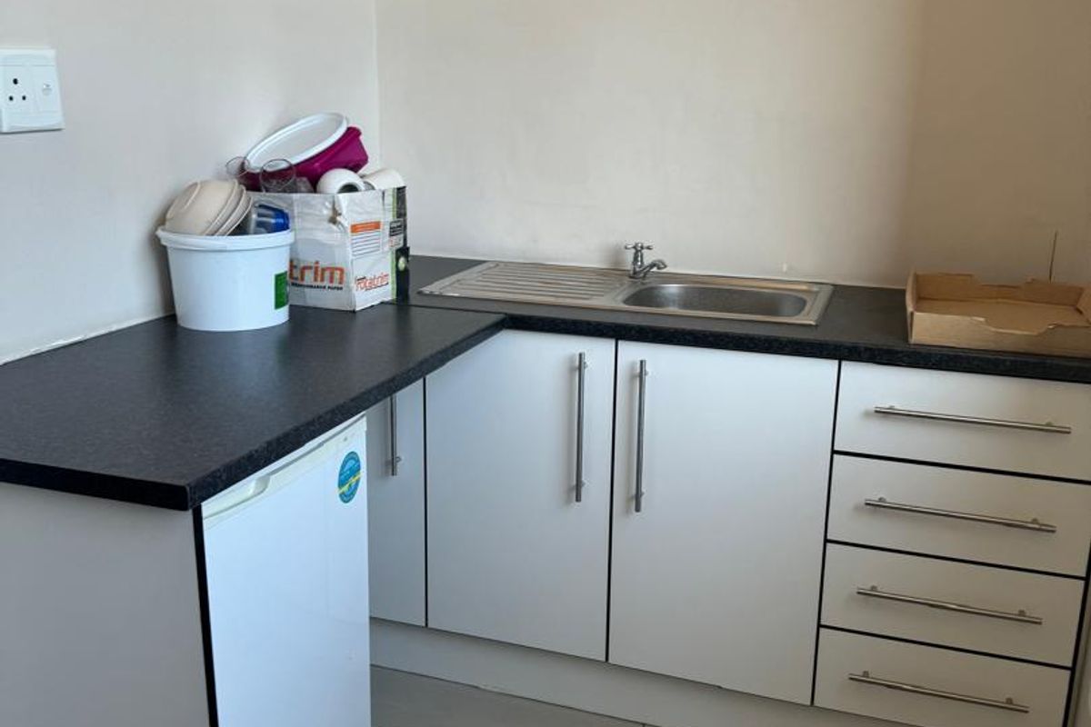 A compact kitchenette area featuring white cabinetry, a dark laminate countertop, and a stainless steel sink with a mixer tap.