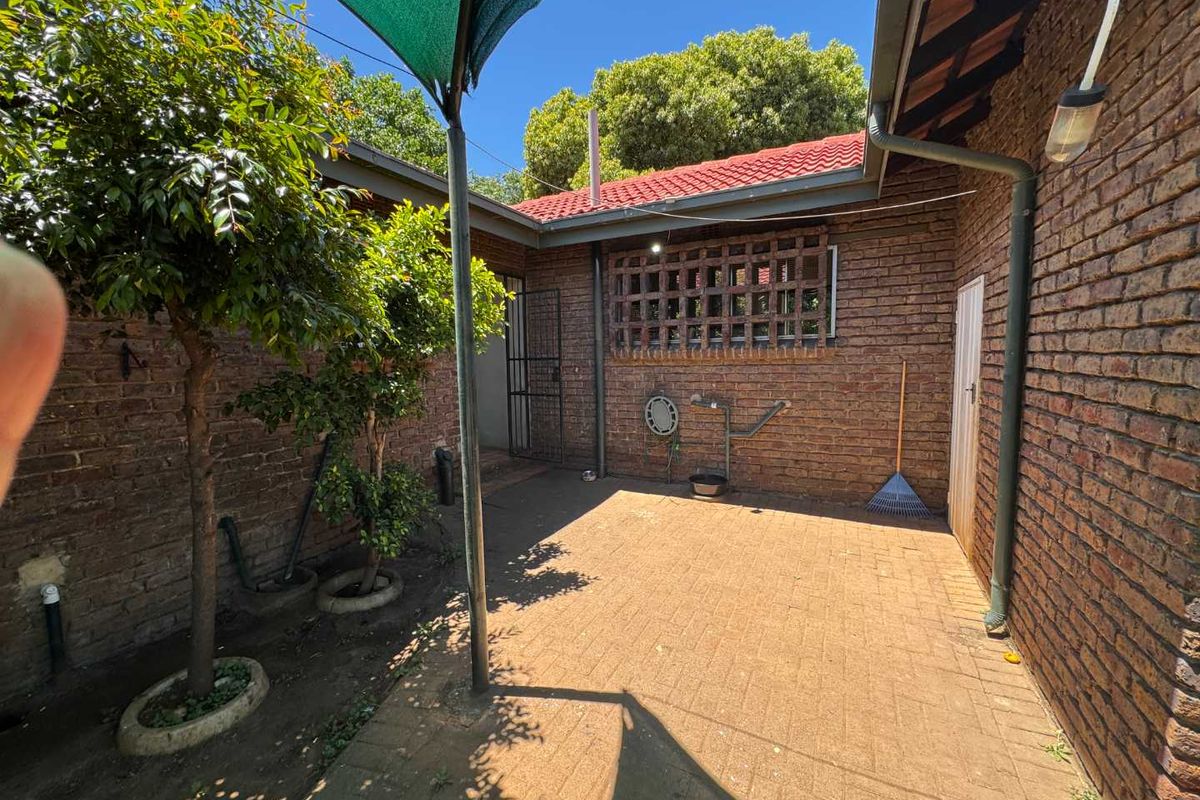 A paved rear courtyard area featuring exposed brick walls, a security gate, and a shade sail, providing a functional outdoor space.