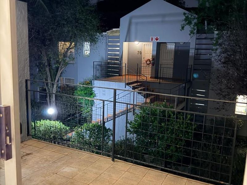A night view from a balcony overlooking an exterior courtyard area with metal railings and tiled flooring.