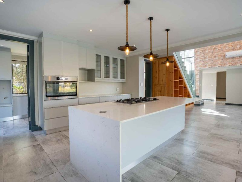 Modern open-plan kitchen featuring a large central island with gas cooktop, built-in oven, sleek cabinetry, and stylish pendant lighting, set against an exposed brick feature wall.