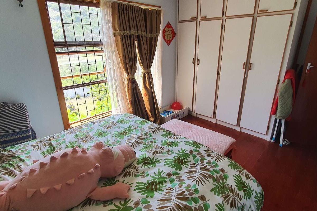 A bedroom featuring built-in wardrobes, wooden flooring, and a window with security bars overlooking the exterior.