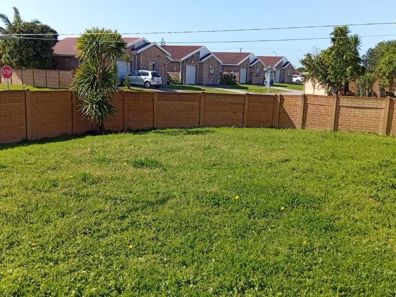 A spacious, open grass garden area enclosed by a precast concrete boundary wall, offering a clear view of the surrounding townhouse complex.