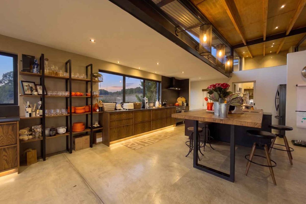 Modern open-plan kitchen featuring polished concrete floors, custom timber cabinetry, a large central island, and exposed timber beams with integrated lighting.