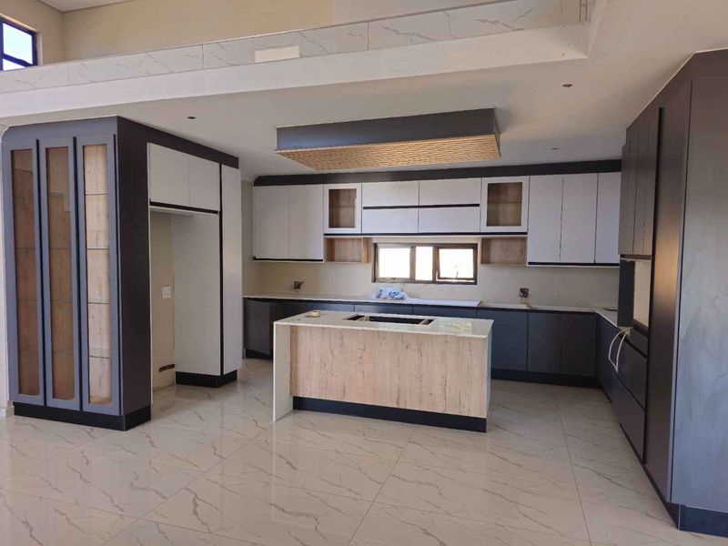 Modern, spacious kitchen featuring two-tone cabinetry, a central island with integrated cooktop, and large-format marble-look floor tiles in a contemporary open-plan layout.