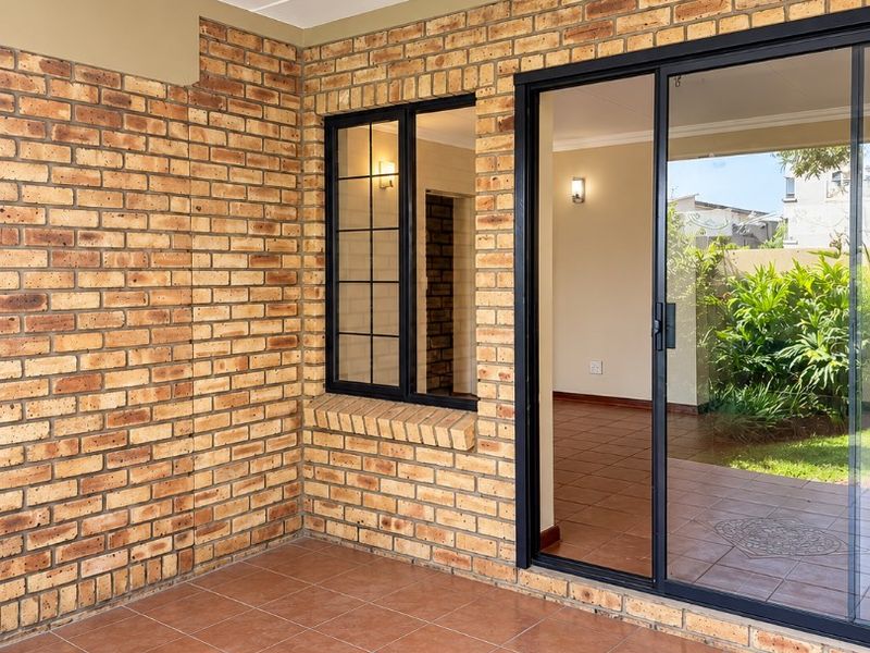 A covered patio area featuring exposed brick walls, tiled flooring with a decorative inlay, and a large sliding glass door leading to the interior.