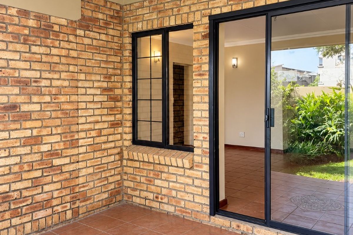 A covered patio area featuring exposed brick walls, tiled flooring with a decorative inlay, and a large sliding glass door leading to the interior.