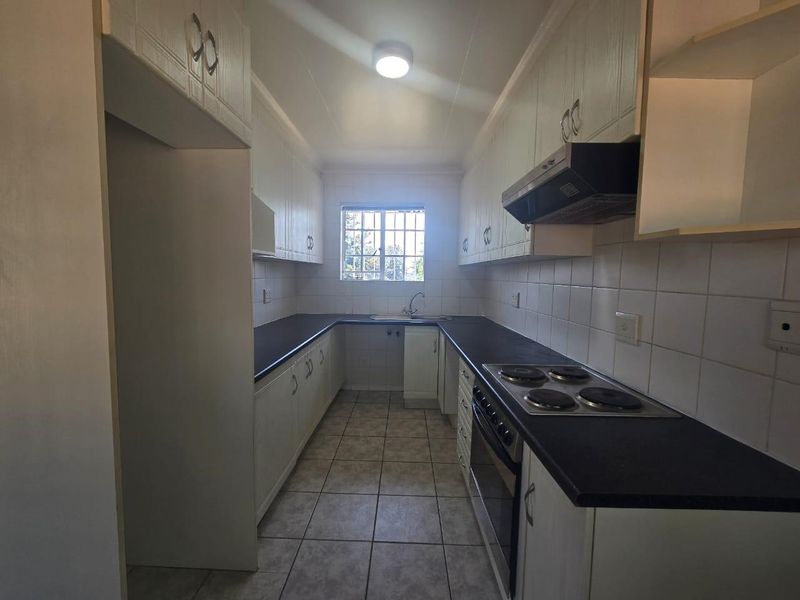 A functional galley-style kitchen featuring white cabinetry, dark laminate countertops, built-in electric oven and hob, and tiled flooring.