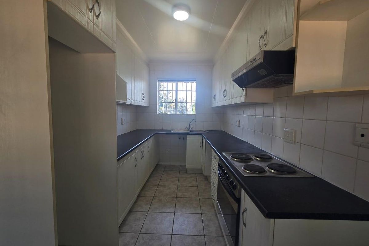 A functional galley-style kitchen featuring white cabinetry, dark laminate countertops, built-in electric oven and hob, and tiled flooring.