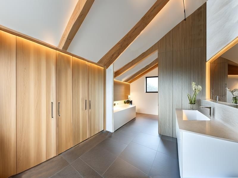 Modern luxury bathroom featuring exposed timber beams, extensive built-in cabinetry, integrated LED lighting, a sleek vanity basin, and a freestanding bathtub.