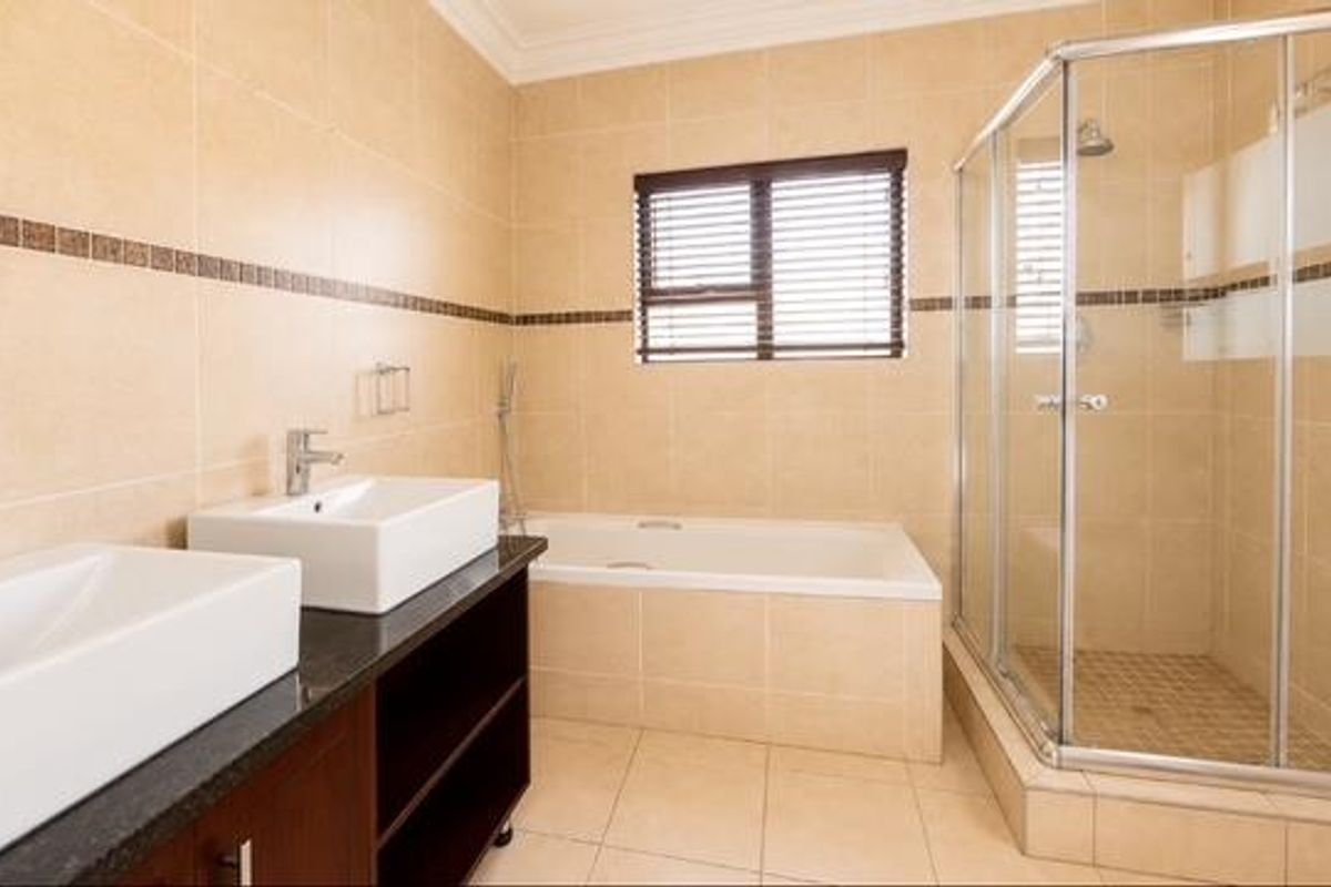 Spacious bathroom featuring a double vanity with vessel sinks, a built-in bathtub, and a separate corner shower enclosure with neutral wall tiling.