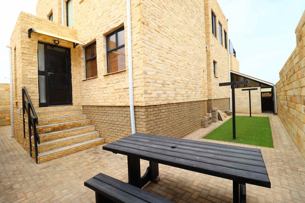 A well-maintained rear exterior area featuring stone cladding, a paved patio, and a small artificial lawn section.