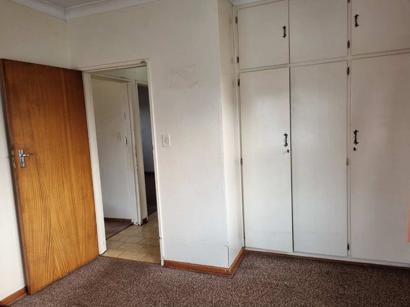 A vacant bedroom featuring built-in cupboards, a wooden door, and carpeted flooring, offering a blank canvas for renovation or restyling.