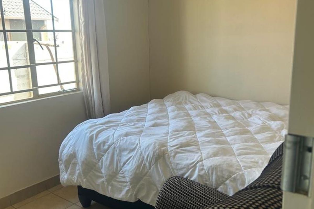 A functional bedroom featuring tiled flooring and a large grid-pattern window allowing natural light into the space.