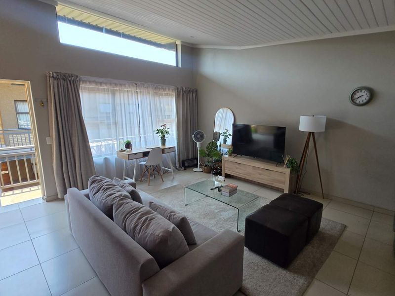 Spacious open-plan living area featuring high raked ceilings, a clerestory window for natural light, and direct access to an outdoor balcony.