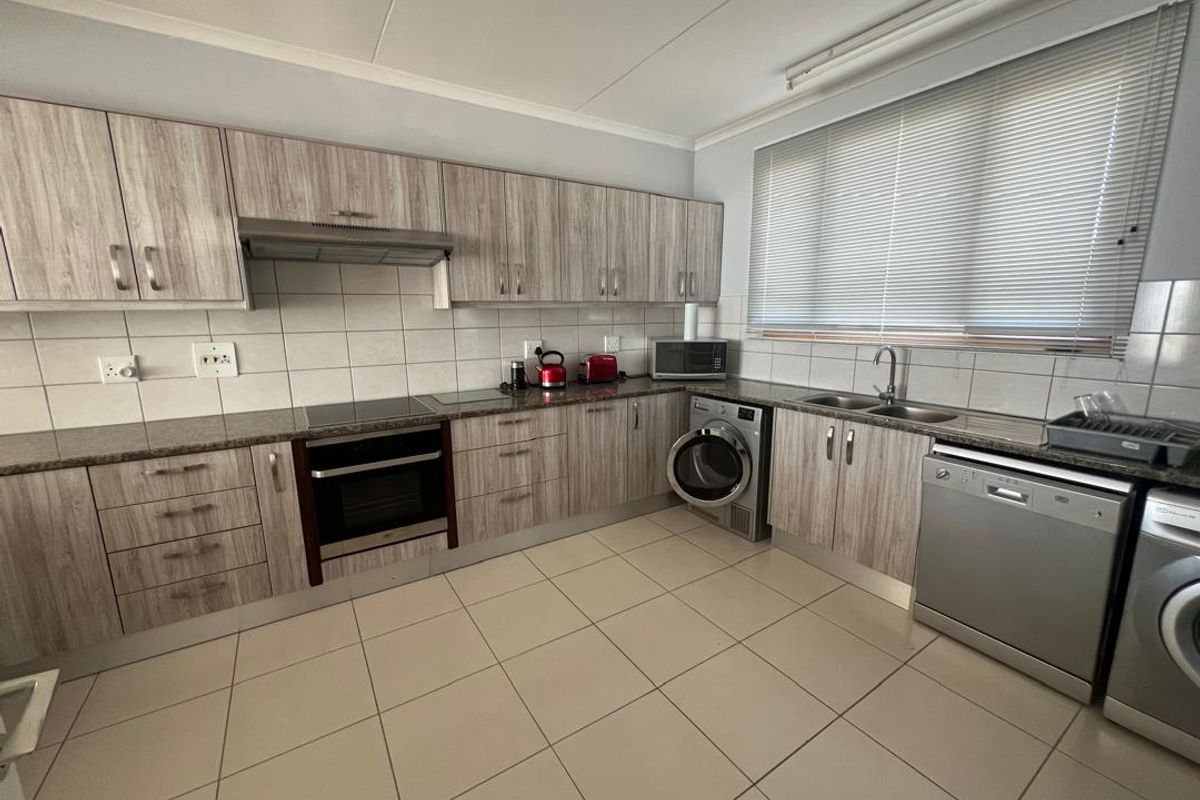A functional kitchen featuring wood-look cabinetry, tiled splashbacks, integrated oven and hob, and dedicated space for laundry appliances.