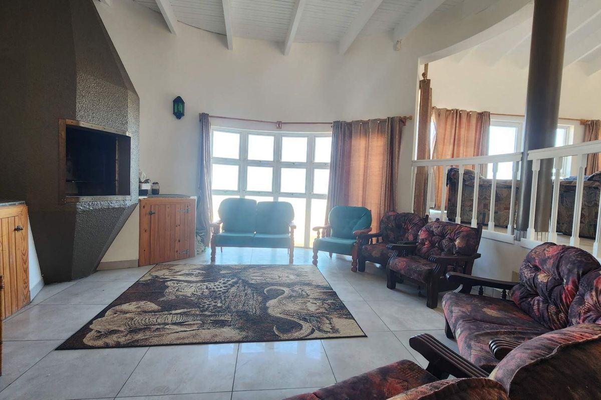 Spacious living room featuring a unique built-in fireplace, tiled flooring, and high exposed beam ceilings with natural light from large windows.