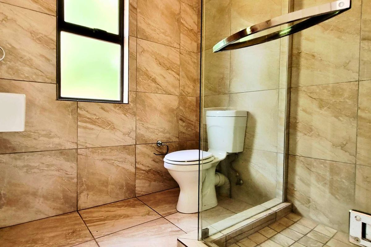 Modern bathroom featuring floor-to-ceiling beige marble-look tiles, a glass-enclosed shower, and a standard toilet.