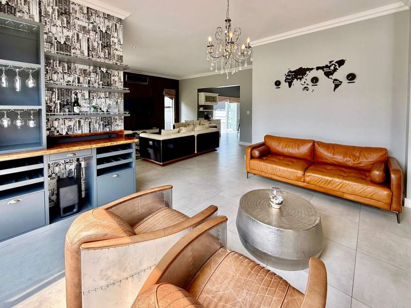 Spacious open-plan living area featuring tiled floors, a built-in bar unit, elegant chandelier lighting, and a seamless flow into the adjacent lounge space.