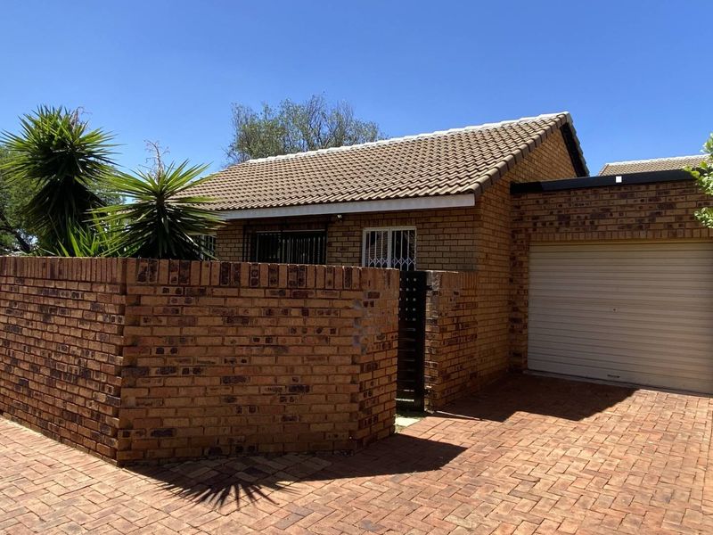 Front view of a face brick townhouse featuring a tiled roof, paved driveway, and a single garage with a secure perimeter wall.