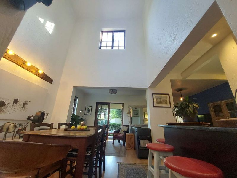Spacious open-plan living and dining area featuring a double-volume ceiling, high-level window, and a breakfast bar connecting to the kitchen.