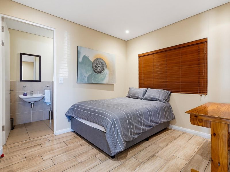 A well-maintained bedroom featuring tiled flooring, wooden venetian blinds, and an adjoining en-suite bathroom with a wall-mounted basin.