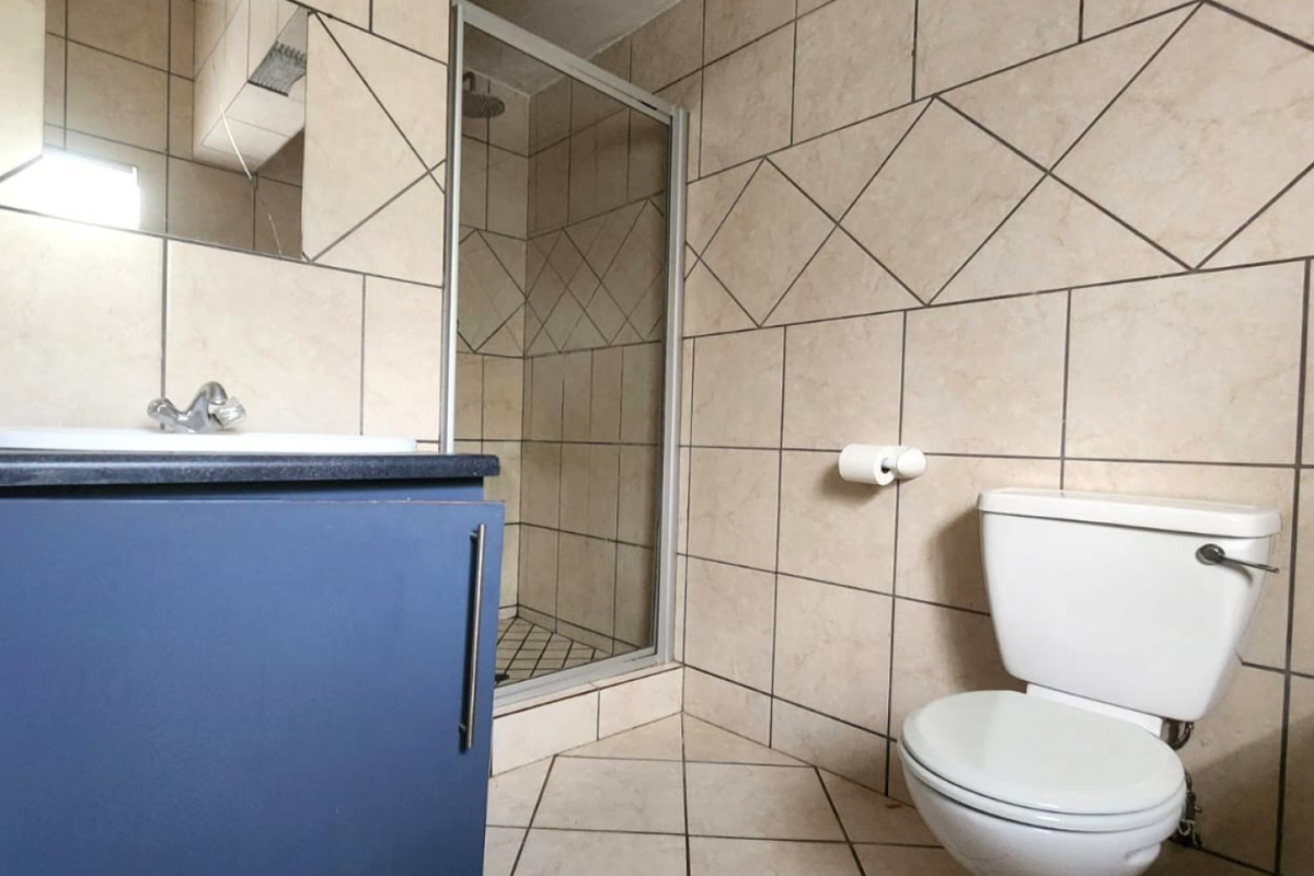 A functional bathroom featuring a shower enclosure, vanity cabinet with basin, and toilet, finished with neutral wall and floor tiling.