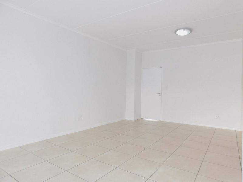 A bright, empty living area featuring neutral tiled flooring and clean white walls, providing a versatile blank canvas for interior design.