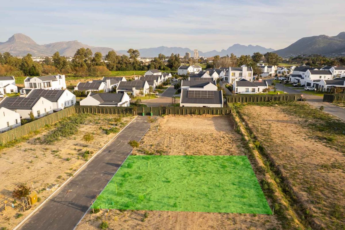 Aerial view of a vacant residential plot in a developed estate, featuring direct road access and surrounding mountain views.