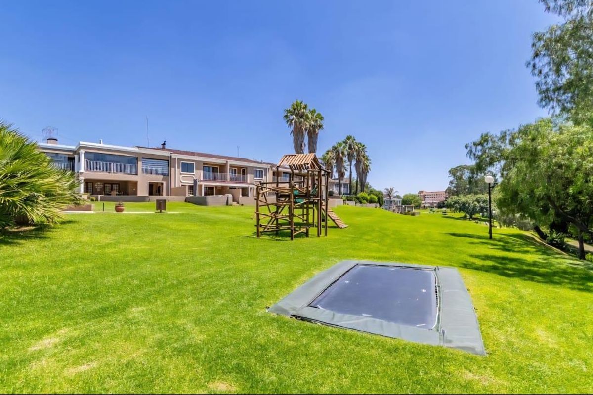 A view of the rear exterior of the townhouse complex, featuring expansive manicured lawns, private balconies, and paved patio areas.