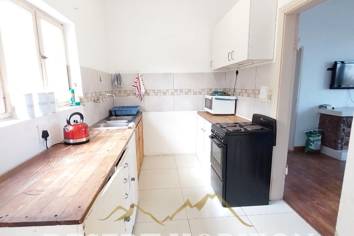 A functional kitchen featuring tiled flooring, wooden countertops, built-in cabinetry, and a freestanding stove, with direct access to the adjacent living area.