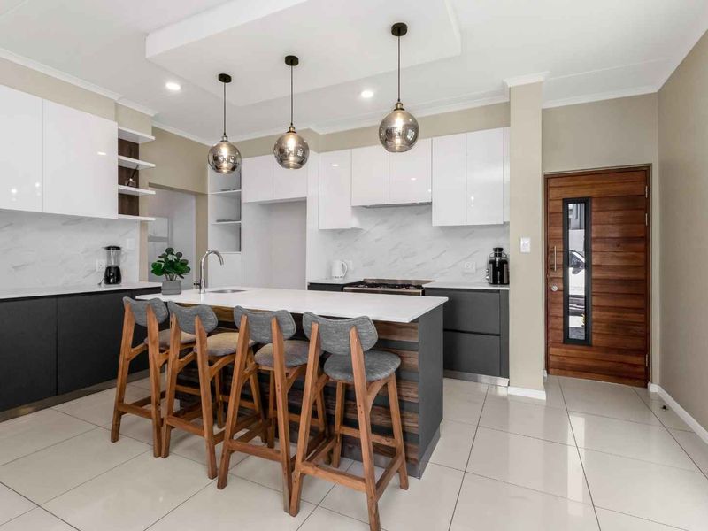 Modern kitchen featuring a central island with breakfast bar, sleek white and charcoal cabinetry, marble-look splashback, and high-quality tiled flooring.