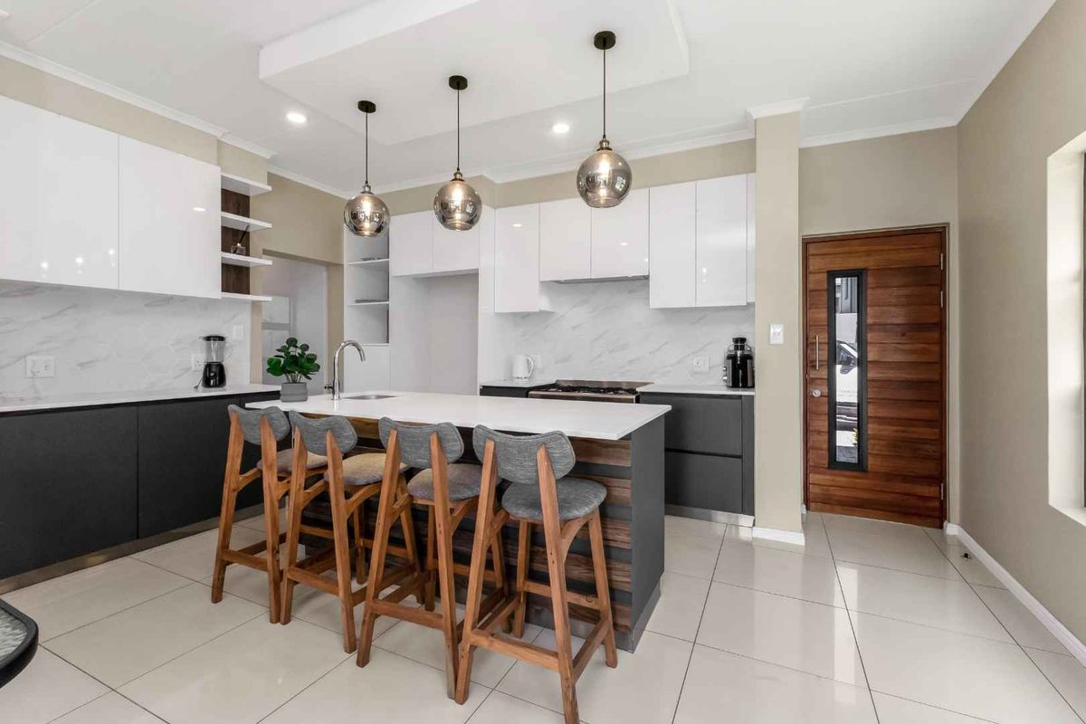 Modern kitchen featuring a central island with breakfast bar, sleek white and charcoal cabinetry, marble-look splashback, and high-quality tiled flooring.