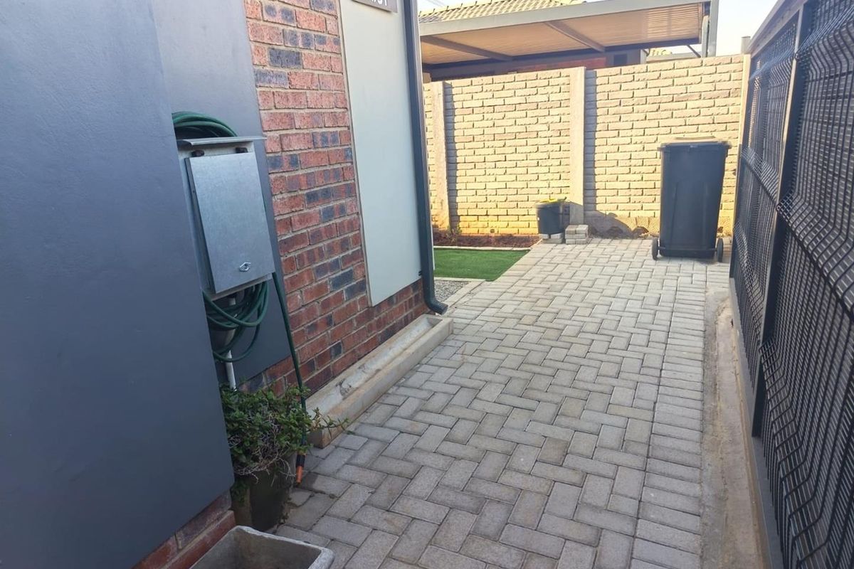 A side exterior walkway featuring brick walling, paved flooring, and secure metal fencing, providing a clean and functional outdoor utility space.
