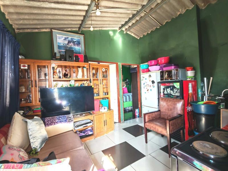 Open-plan living and kitchen area featuring tiled flooring and exposed roof structure, requiring cosmetic updates to improve the overall aesthetic.