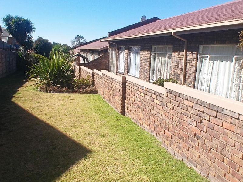 A view of the rear exterior of the townhouse, featuring a brick facade, tiled roof, and a private lawn area with boundary walling.